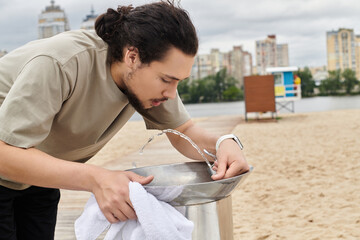 Sporty young man enjoys a refreshing drink while exercising outdoors by the water