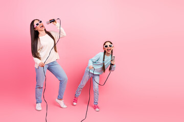 Mom and daughter enjoy singing together, holding microphones and dressed stylishly, sharing a...
