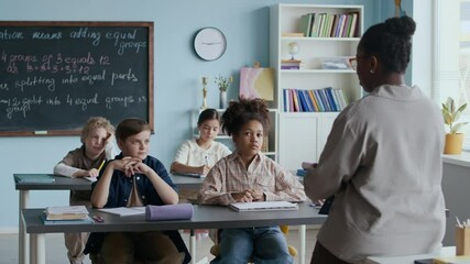 Black female teacher standing in front of young diverse student sitting and listening at their desks during interactive Math lesson in modern classroom - Powered by Adobe