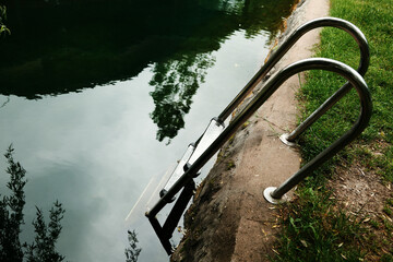 Close-up of a shiny metal ladder descending into clear green water, captured from above....