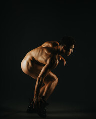 A conceptual image showcasing a male model in a crouched position, illuminated by low-key studio...
