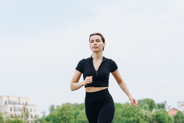 young slim beautiful caucasian woman running on path on river embankment in city park, black...