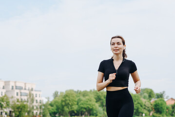young slim beautiful caucasian woman running on path on river embankment in city park, black...