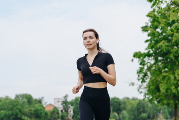 young slim beautiful caucasian woman running on path on river embankment in city park, black...