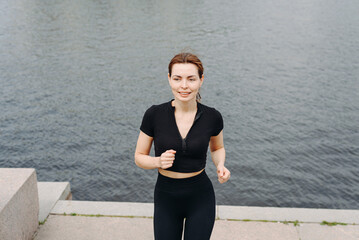 young slim beautiful caucasian woman running on stone stairs on river embankment in city park,...