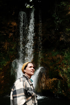 Young woman in plaid jacket enjoying view of Veliki Buk waterfall in Lisine reserve, Serbia country. Serene moment in lush nature by cascading water. Travel concept.
