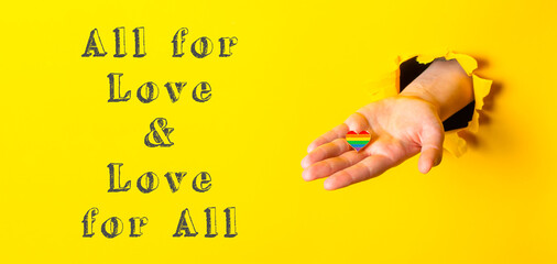 Hand holding a rainbow heart with the words All for Love