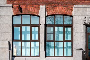 Two rectangular windows with a red brick arch against a grey block wall. From the Windows of the World series.