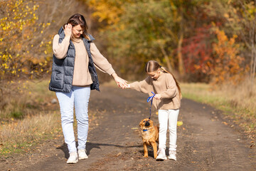 Happy family mother and little daughter walk with golden puppy dog in park on autumn day, excited...
