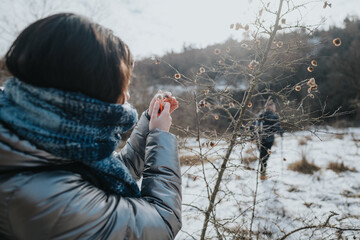A young adventurer photographs nature's details during a chilly hiking excursion in a snowy setting...