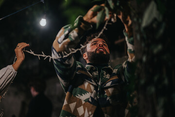 A person hanging decorative lights outdoors during a nighttime celebration, creating a festive and...