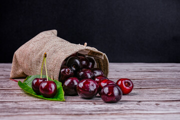 Fresh cherries spill out of a burlap sack onto a wooden table.