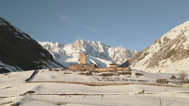 Aerial view Ancient Lamaria Monastery in snowy highland valley, surrounded by Caucasus peaks, part of UNESCO listed Upper Svaneti region
