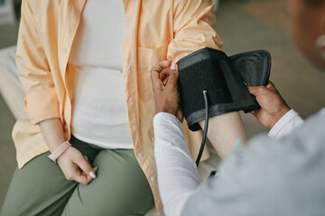 Asian pregnant woman sitting while medical professional checking blood pressure during prenatal...