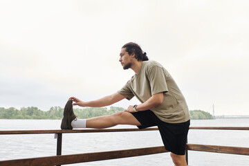Sporty man performs an impressive stretch by the lakeshore at dawn