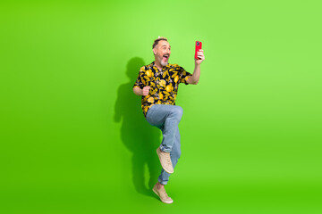 Excited gentleman holding a smartphone while posing against bright green wall in casual summer...