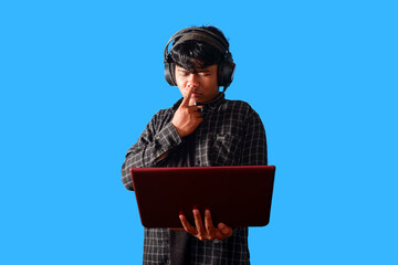 Focused Young Man Using Laptop and Headphones, Concentrated Expression  isolated on blue background