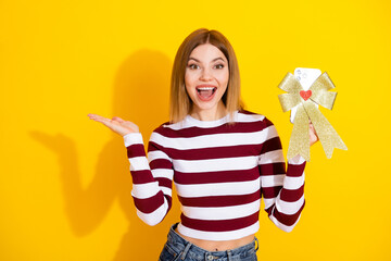 Excited young woman in casual attire presenting a gift wrapped smartphone with vibrant yellow...