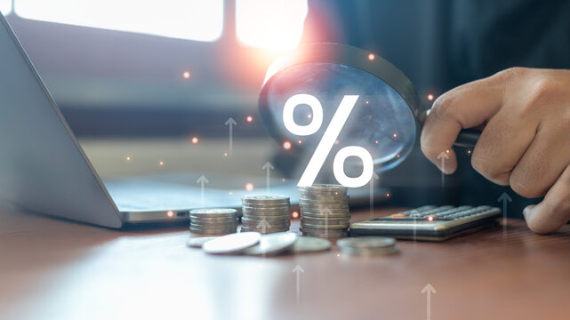 Close-up of stacked coins with a magnifying glass focusing on a percentage sign.