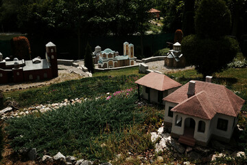 Miniature models of Serbian village houses and historic churches arranged on a grassy slope in an...