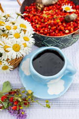 A blue cup of black coffee with red wild strawberries, a bouquet of white daisies. outdoor summer picnic