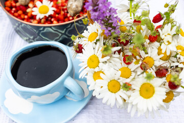 A blue cup of black coffee with red wild strawberries, a bouquet of white daisies. outdoor summer...