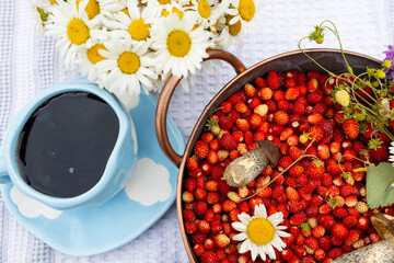 A blue cup of black coffee with red wild strawberries, a bouquet of white daisies. outdoor summer...