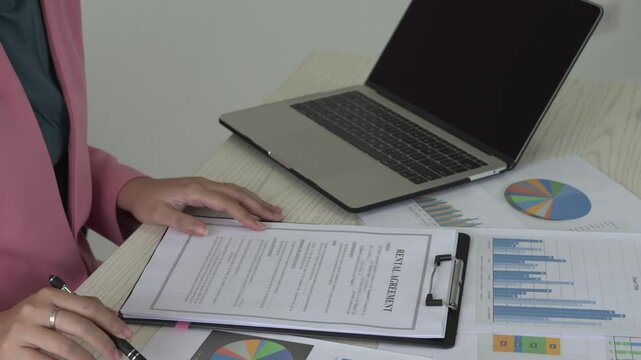 Real estate gent asian woman is reading and checking paper documents, signing the contract to send to her business partner. Concentrated smart ambitious lady is preparing research, remote freelancer.