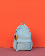 A backpack with colored pencils against vibrant orange wall – back to school concept