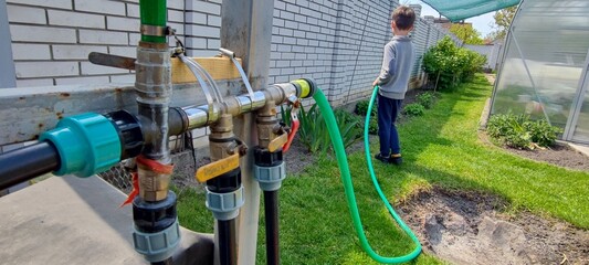 Child watering backyard garden with hose on sunny day. sustainable lifestyle and outdoor activity...
