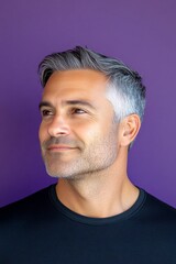 Obraz premium A glowing and peaceful man expressing warmth. Idea of style for aging men. Purple solid background. Fashionable men's shoulder-length taper haircut - midlife white man with grey hair.