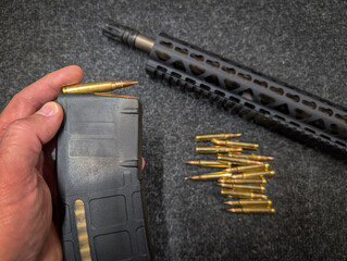 A man's hand loads a magazine for a modern tactical rifle with 5.56x45mm caliber ammunition....