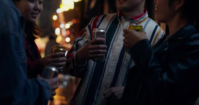 A group of young people are drinking beer on a city street. They laugh and clink cans together.