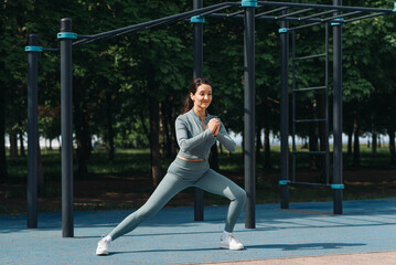 young athletic caucasian woman doing stretching exercises outdoors in summer, grey sportswear,...