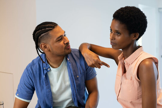 Talking couple pointing to chest while sitting in bright white home kitchen, natural light - Powered by Adobe
