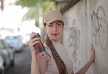 young woman with spray can in front of graffiti