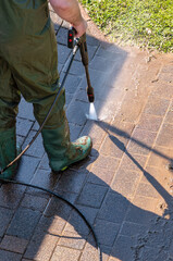 Garden patio being cleaned with water jet – spring cleaning outdoors. A man cleans a heavily soiled stone terrace using a high-pressure washer.
