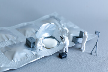 Creative conceptual image showing tiny figurines of forensic investigators examining a pill on an...