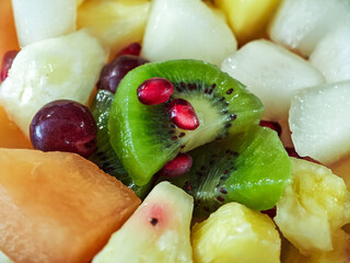 A fruit bowl with kiwi, grapes, melon, pineapple, and pomegranates