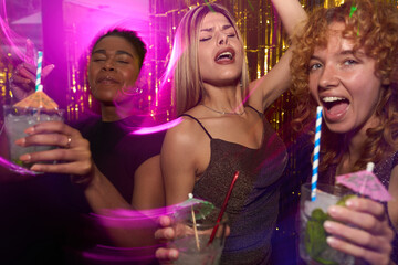 Young women holding cocktails dancing at nightclub party
