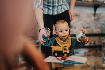 A young child seated at a table playing with a toy truck and holding objects, supported by a parent...