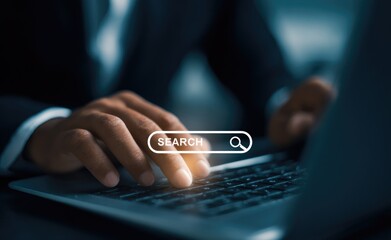 Close-up of businessman's hands typing on laptop keyboard with virtual screen showing search bar and magnifying glass icon