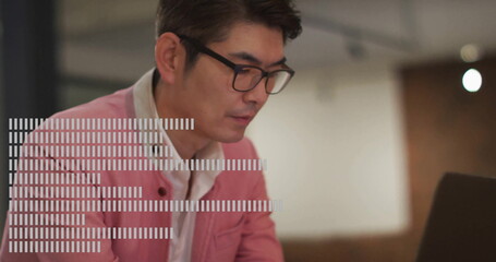 Focusing Asian man wearing pink blazer typing on laptop at modern office desk, with eyeglasses