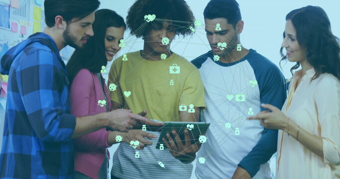 Team members collaborating around tablet in studio, visualizing network icons with whiteboard notes