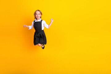 Obraz premium Cheerful young schoolgirl jumping with joy on a vibrant yellow background, celebrating education and childhood energy