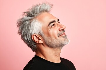Obraz premium Classy men's spiky hair haircut - midlife middle eastern man with middle hair. Pink solid background. A modern and graceful man smiling naturally. Idea of style for aging men.