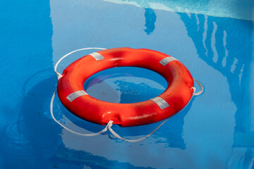 Red lifebuoy floating on the surface of a clear blue swimming pool, closeup. Summer image...