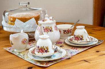 Bone china teapot, tea cups, milk jug and sugar bowl on a wooden table together with a Victoria sponge cake