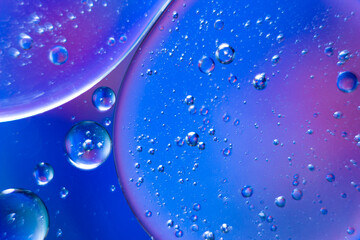 Air bubbles trapped in oil droplets floating on the surface of water with a colorful background, selective focus.