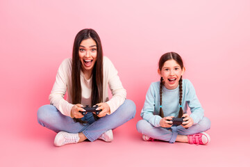 Mother and daughter enjoying gaming together on pink background reflecting joy and bonding through...